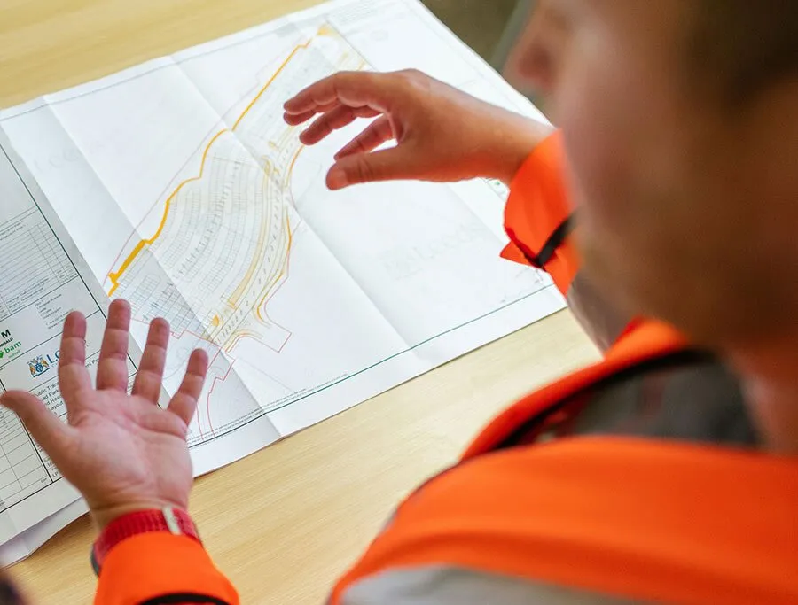 Person in Warnjacke prüft einen Bauplan am Tisch