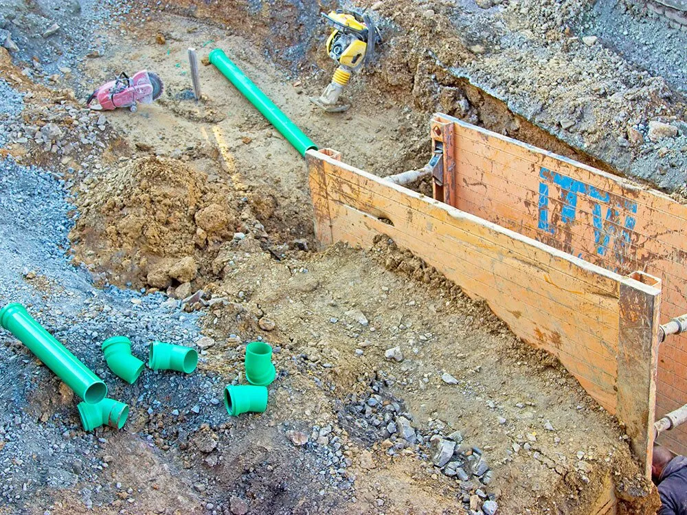 Rohrgraben mit Verbau und grünen Kanalrohren auf einer Baustelle