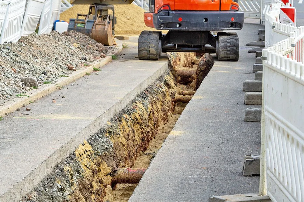 Bagger hebt einen Graben neben einem Gehweg aus